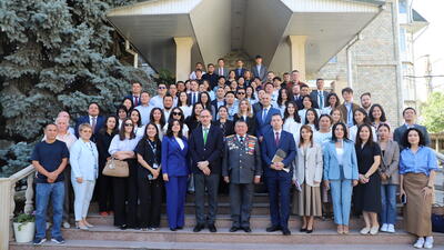 Large group of people posing on steps outside a building, some in suits and uniforms, with greenery in the background.
